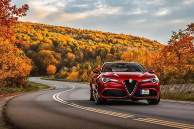 Une Alfa Romeo Stelvio rouge stationnée sur une route sinueuse avec des feuilles d'automne colorées en arrière-plan.