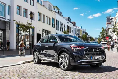 La nouvelle Audi Q3 2025 est stationnée dans une rue urbaine animée sous un ciel bleu.