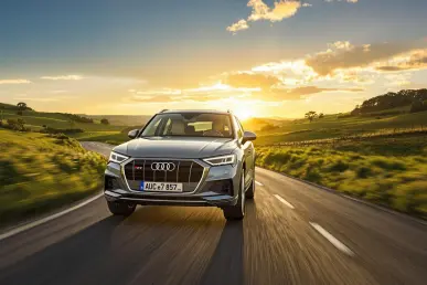 Une Audi Q5 e-hybrid roule sur une route de campagne au coucher du soleil.