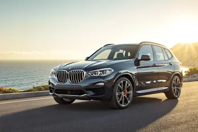 La BMW iX3 Neue Klasse garée sur une route côtière avec l'océan en arrière-plan.