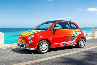 La Fiat Topolino Vilebrequin est stationnée sur une route côtière ensoleillée, avec la mer bleue en arrière-plan.