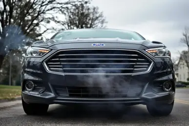 Une voiture Ford avec de la fumée s'échappant du capot dans un quartier résidentiel.