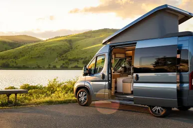 Un camper-van Furgok bleu métallisé garé près d'un lac au coucher du soleil.