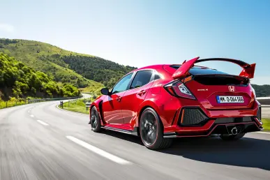 La Honda Civic Type R Ultimate Edition roule sur une route sinueuse européenne, entourée de collines verdoyantes sous un ciel bleu.