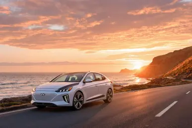 La Hyundai Ioniq 9, un SUV électrique 7 places, est stationnée sur une route côtière avec l'océan en arrière-plan sous une lumière dorée.
