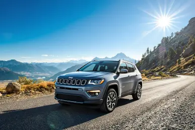 La Jeep Compass 2025 est garée sur une route de montagne pittoresque avec un ciel bleu clair.