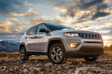 Un Jeep Compass 4xe stationné sur un terrain rocheux avec des montagnes en arrière-plan au coucher du soleil.