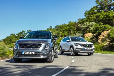 Les SUV électriques Kia EV3 et Skoda Elroq sur une route sinueuse entourée de verdure.