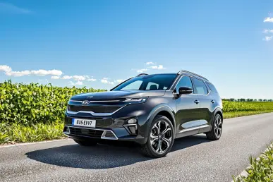 La KIA EV5 SUV est garée sur une route de campagne française, entourée de champs verts et sous un ciel bleu clair.