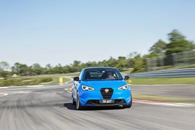 Une Lancia Ypsilon HF électrique bleue prend un virage sur circuit sous un ciel clair.
