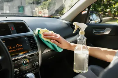 Une personne nettoie un tableau de bord de voiture avec un chiffon en microfibre et un spray naturel.