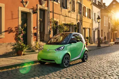 Une petite voiture électrique colorée stationnée dans une rue européenne pittoresque au coucher du soleil.