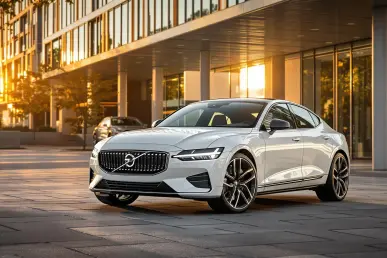 La Polestar 2 blanche se tient devant un paysage urbain moderne au coucher du soleil.