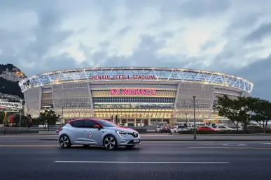 La Renault 4 électrique est stationnée devant le stade de l'AS Monaco, illuminé en soirée.