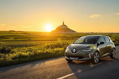 Une Renault 5 électrique stationnée sur une route pittoresque en Normandie, avec Mont Saint-Michel.