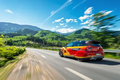 La Renault 5 Turbo 3E roule sur une route de montagne pittoresque, soulignant son design moderne et vibrant.