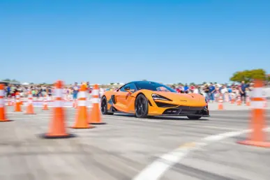 Une voiture de sport colorée navigue à travers des cônes sur une piste ensoleillée.