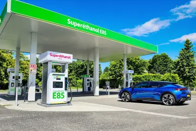 Une voiture moderne bleue stationnée à une pompe de Superéthanol E85 sous un ciel bleu.