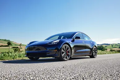 Une Tesla Model 3 est garée sur une route rurale, entourée de collines et d'un ciel bleu.