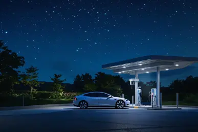 Une voiture électrique moderne se recharge la nuit sous un ciel étoilé.