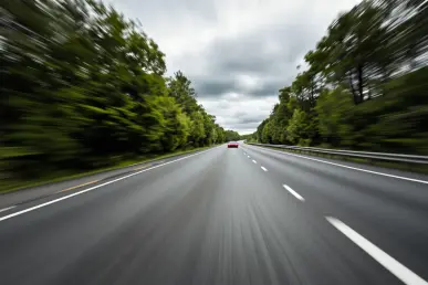 Une voiture de sport rouge fonce sur l'autoroute, entourée de paysages flous.