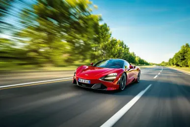 Une voiture de sport rouge filant à grande vitesse sur une autoroute française, entourée de verdure.