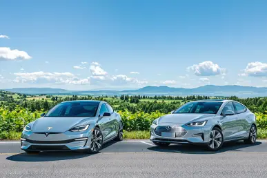 Deux voitures, électrique et hybride, garées sur une route de campagne entourée de verdure.
