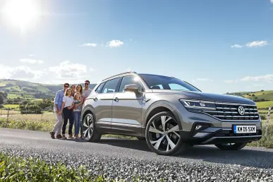 Le Volkswagen Tayron eHybrid 272 ch est garé dans un cadre champêtre avec une famille joyeuse à côté.