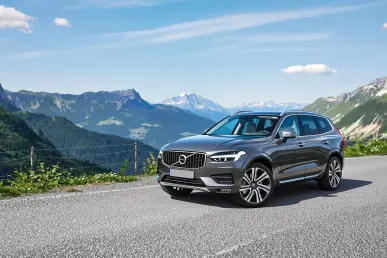 Le Volvo XC70 2025 est stationné sur une route de montagne, avec une vue dégagée sur une vallée verdoyante, sous un ciel bleu clair.