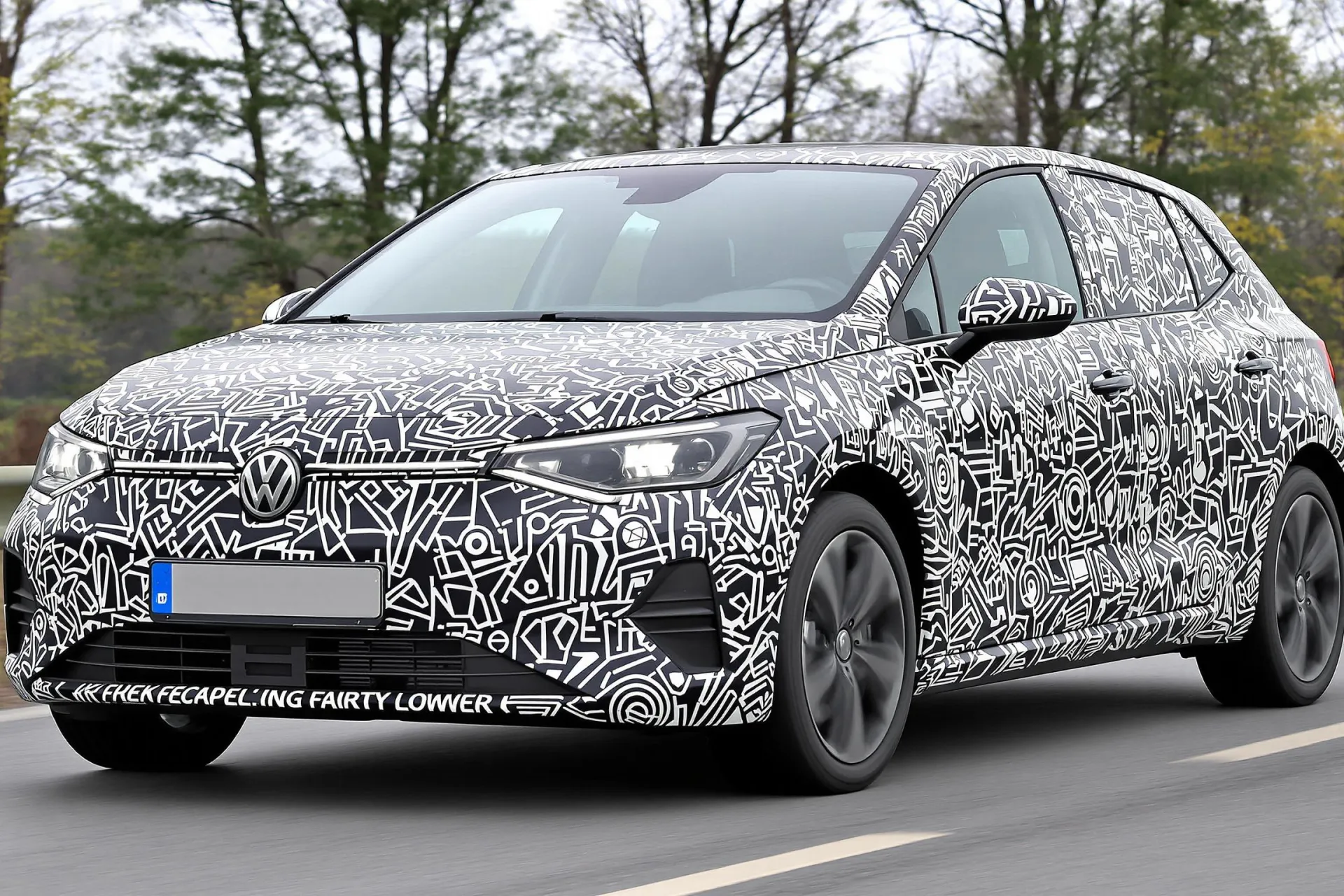 Un prototype de la Volkswagen ID.2 électrique camouflé en Polo circule sur une route allemande pendant ses essais, avec des autocollants imitant les phares et la calandre.