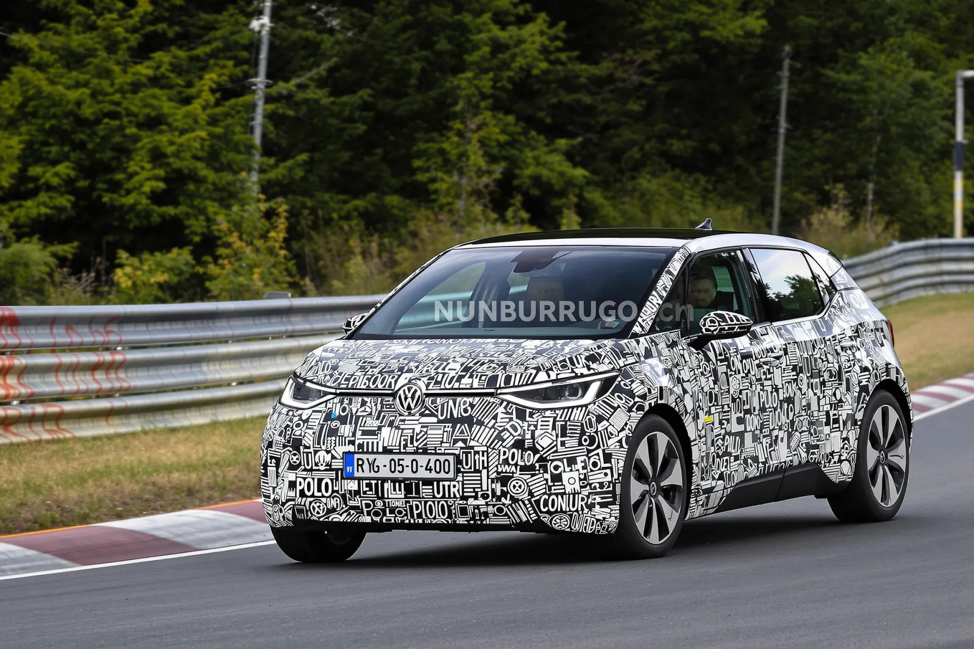 Un prototype de la Volkswagen ID.2 partiellement camouflé négocie un virage sur le circuit du Nürburgring, révélant ses lignes compactes et dynamiques.